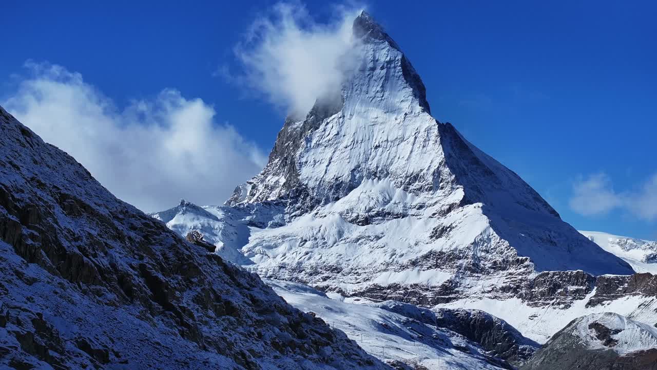 The Matterhorn famous mountain peak rocky cliffs Riffelsee Lake Zermatt Swiss Alps aerial drone wind fog first fresh snow fall autumn winter blue skies morning Gornergrat railway Switzerland upward