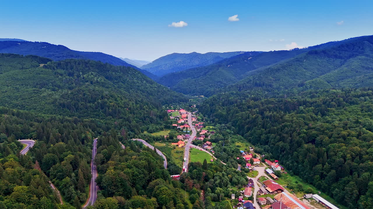 Scenic overview of lush valley with quaint village. Lush green hills surround a charming village nestled in a tranquil valley under a clear blue sky