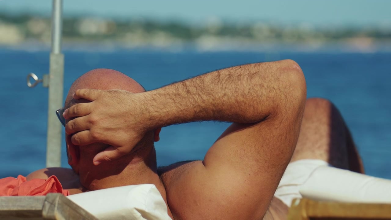 Relaxed man sunbathing on a beach lounger by the sea, enjoying a warm and tranquil coastal vacation day