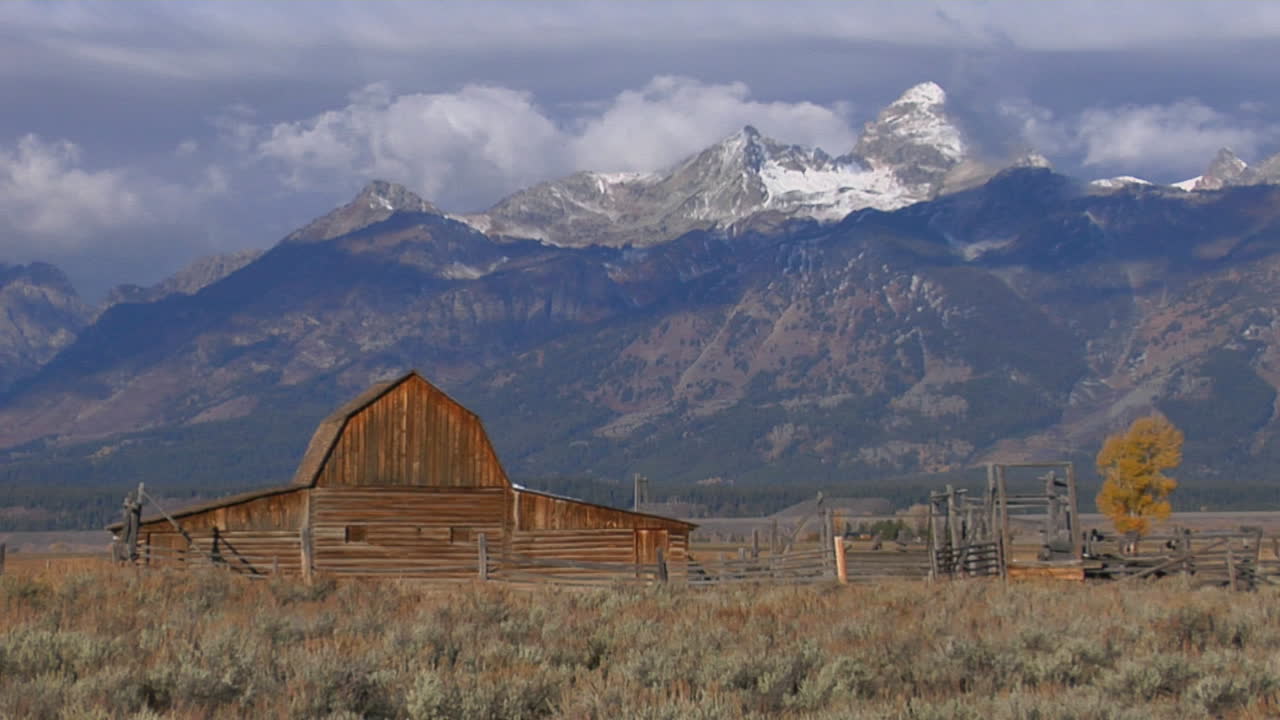 un viejo granero se eleva en una pradera con los grand tetons al fondo 5
