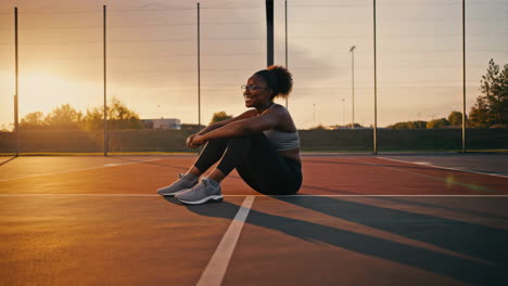 young woman resting on a sports court at sunset