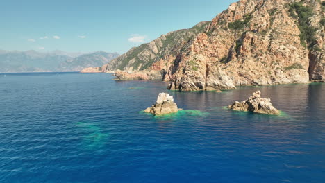 Clear-blue-waters-by-the-Golf-de-Girolata,-Corsica-with-rugged-cliffs-in-the-afternoon-sunlight,-aerial-view