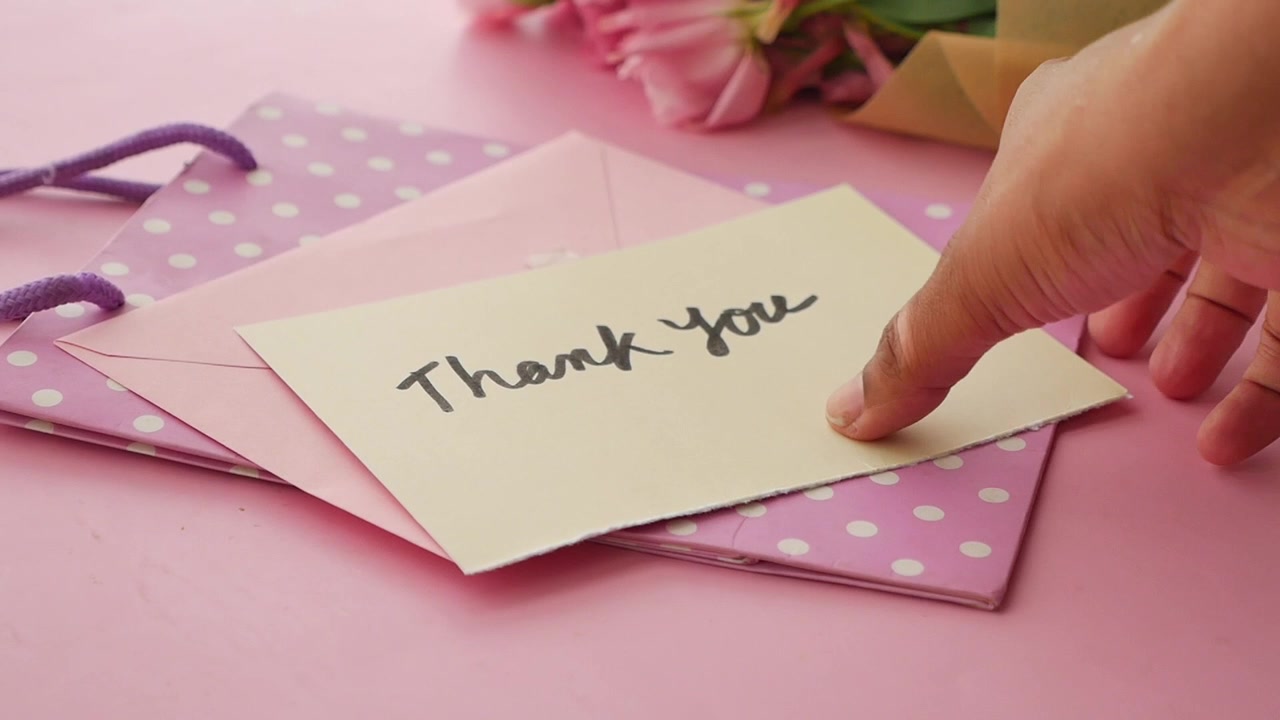 Hand Picking Up a Thank You Note from a Pink Envelope