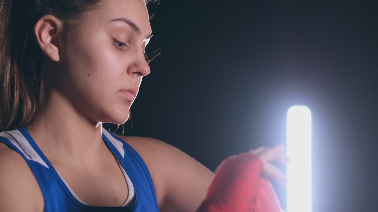 plan medio hermoso boxeador atlético en ropa azul bobinas vendajes rojos en las manos de una luchadora. steadicam tiro