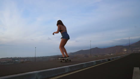 Against-the-backdrop-of-mountains,-a-beautiful-and-stylish-skateboarder-skates-in-shorts-along-a-mountain-road-at-sunset,-all-captured-in-slow-motion