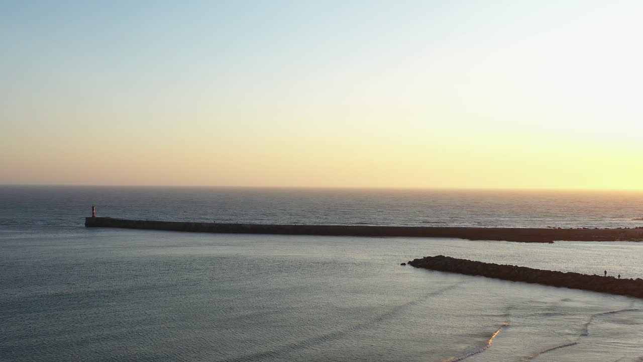 Aerial tracking shot of sunset over ocean and breakwater, Azurara beach