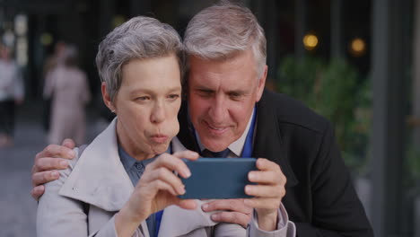 portrait happy middle aged caucasian couple using smartphone taking selfie photos posing enjoying making faces having fun together in city slow motion spontaneous carefree