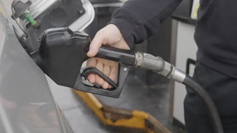 gasolinera hombre caucásico blanco con anillo de bodas llenando coche plateado insertando la boquilla de gas en el tanque y luego ajustando el mecanismo automático de la bomba y retrocediendo