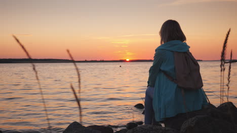 a lonely woman sits on a rock near a picturesque lake at sunset