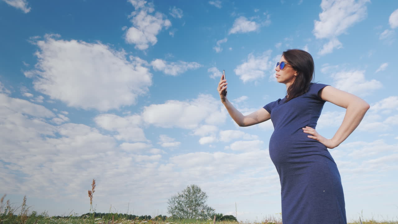 беременная женщина фотографируется на фоне голубого неба