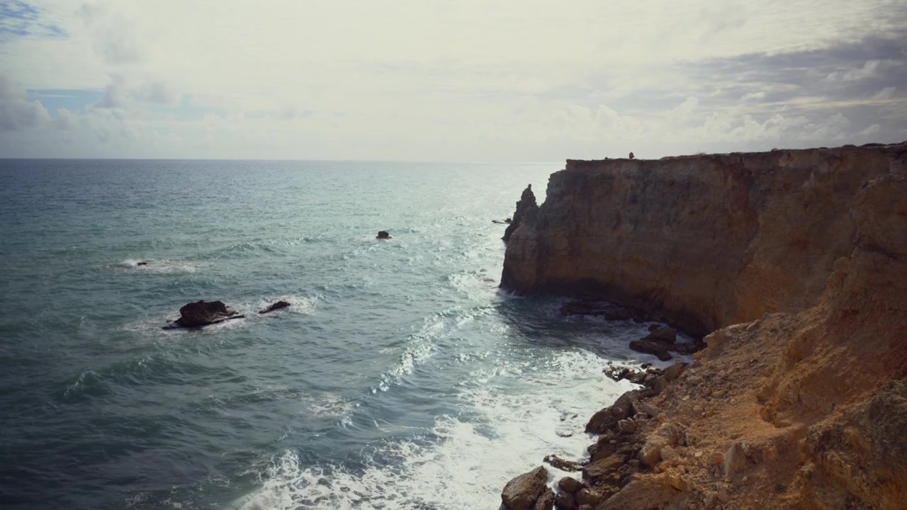 shot of sea waves splashing against rocky cliffs and natural rock arches along the coast on a sunny day.