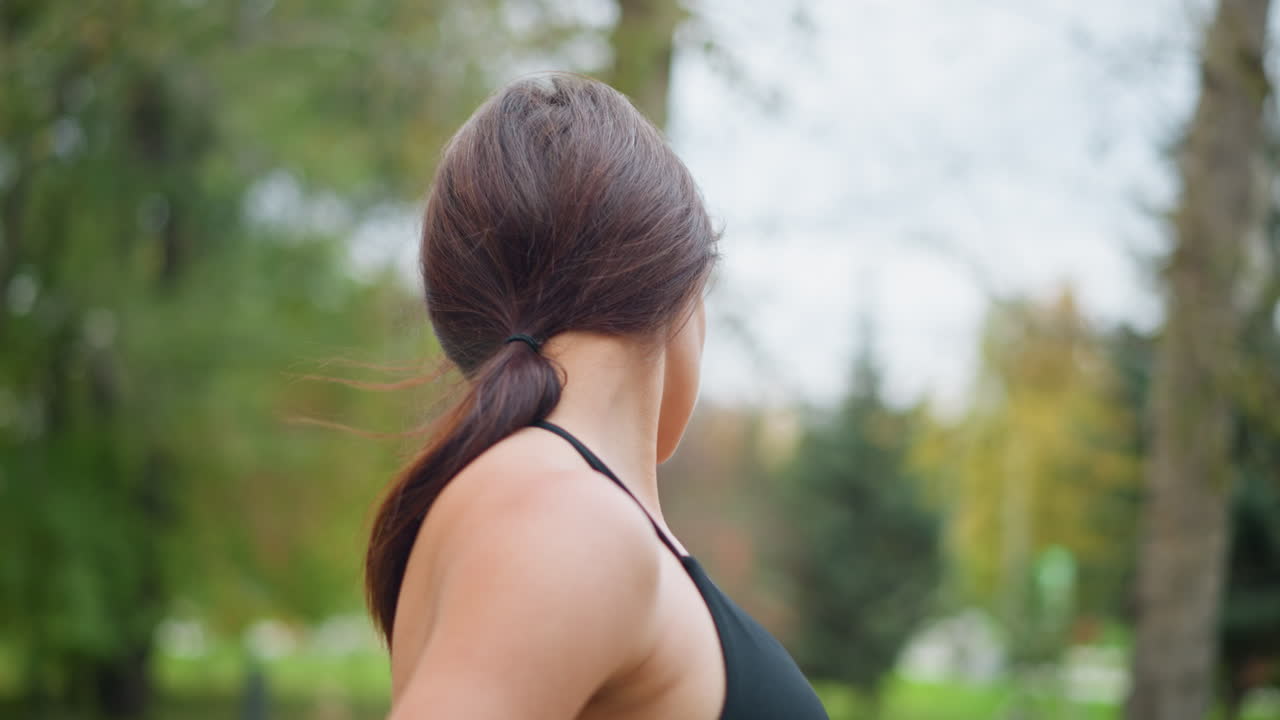 Sport woman stretching neck to ensure flexibility in park, blurred background of trees and leaves, healthy lifestyle, outdoor exercise, neck stretch, fitness routine, focus on neck mobility