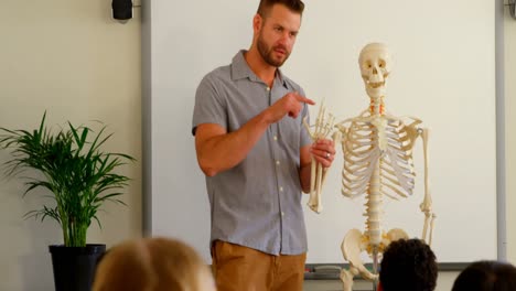 maestro masculino caucásico explicando el modelo de esqueleto en el aula de la escuela 4k