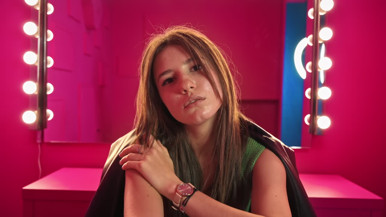 Giovane donna che posa in uno studio con pareti e mobili rosa. Specchio con lampade