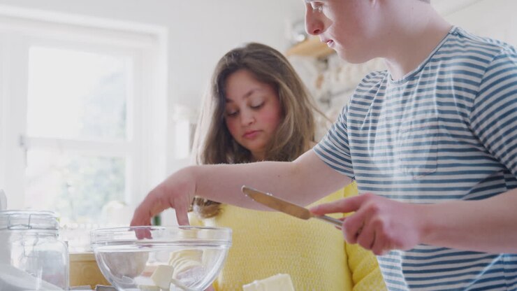 Young Downs Syndrome Couple Adding Butter To Cake Recipe They Are Baking In Kitchen At Home