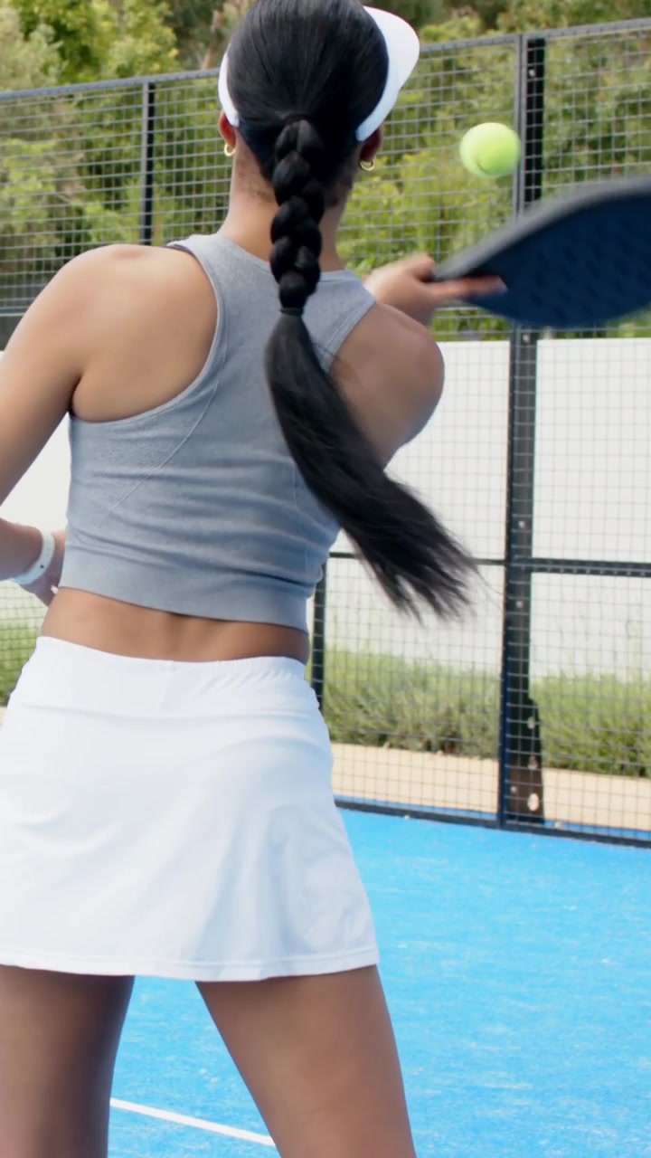 Vertical video: Ball coming, woman in gray top lunging with paddle to return shot on blue court