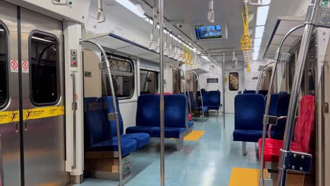 empty subway train interior with blue seats, red handrails, and information screens