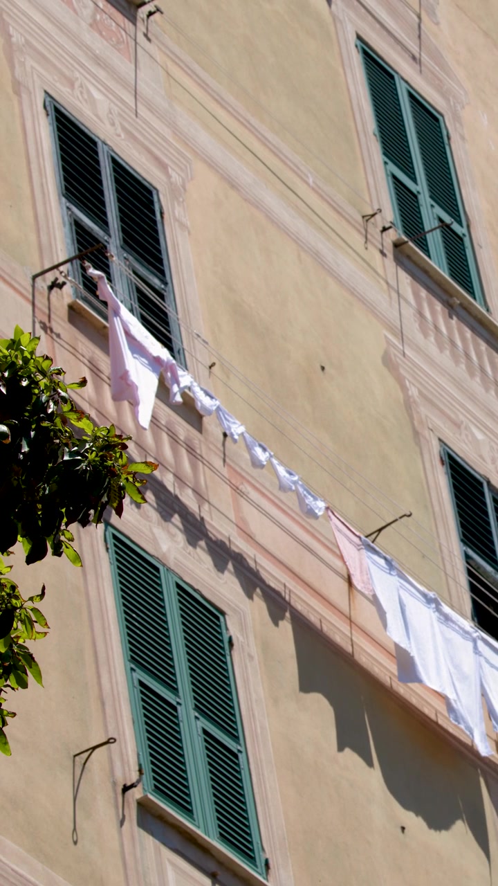 Una cámara en ángulo bajo panea hacia abajo por la fachada de un edificio alto con ropa secándose en tendederos.