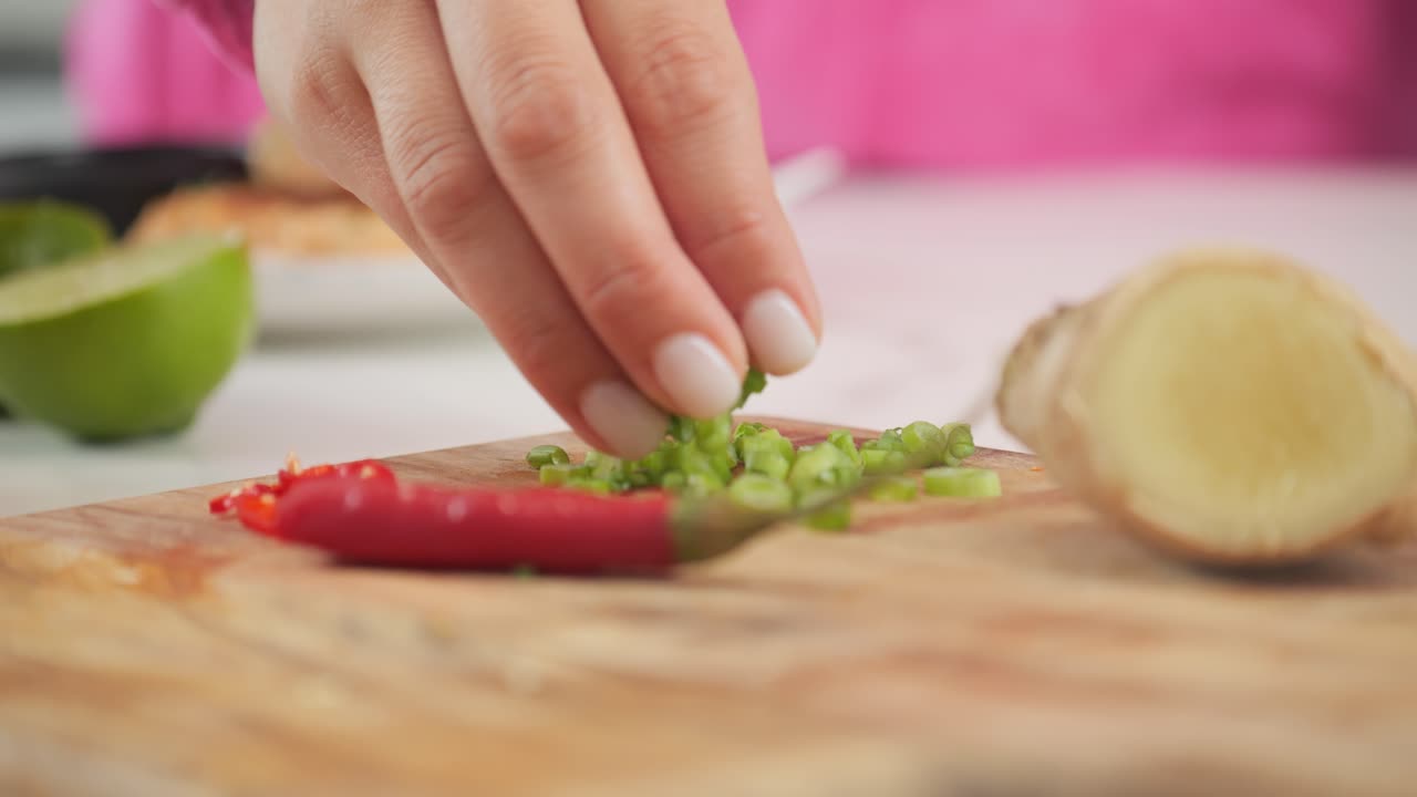Close-up of a cutting board with ingredients and a woman grabs fresh cut green onion while cooking