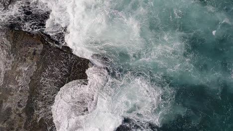 aerial top-down rising over sea waves crashing on rocky coast