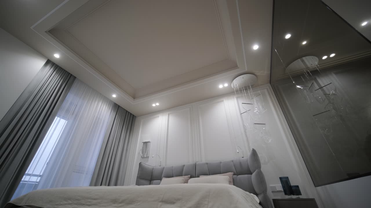 baño elegante y moderno visto desde un dormitorio, que muestra un espejo ovalado con iluminación de fondo, una bañera independiente y una ducha con azulejos geométricos.