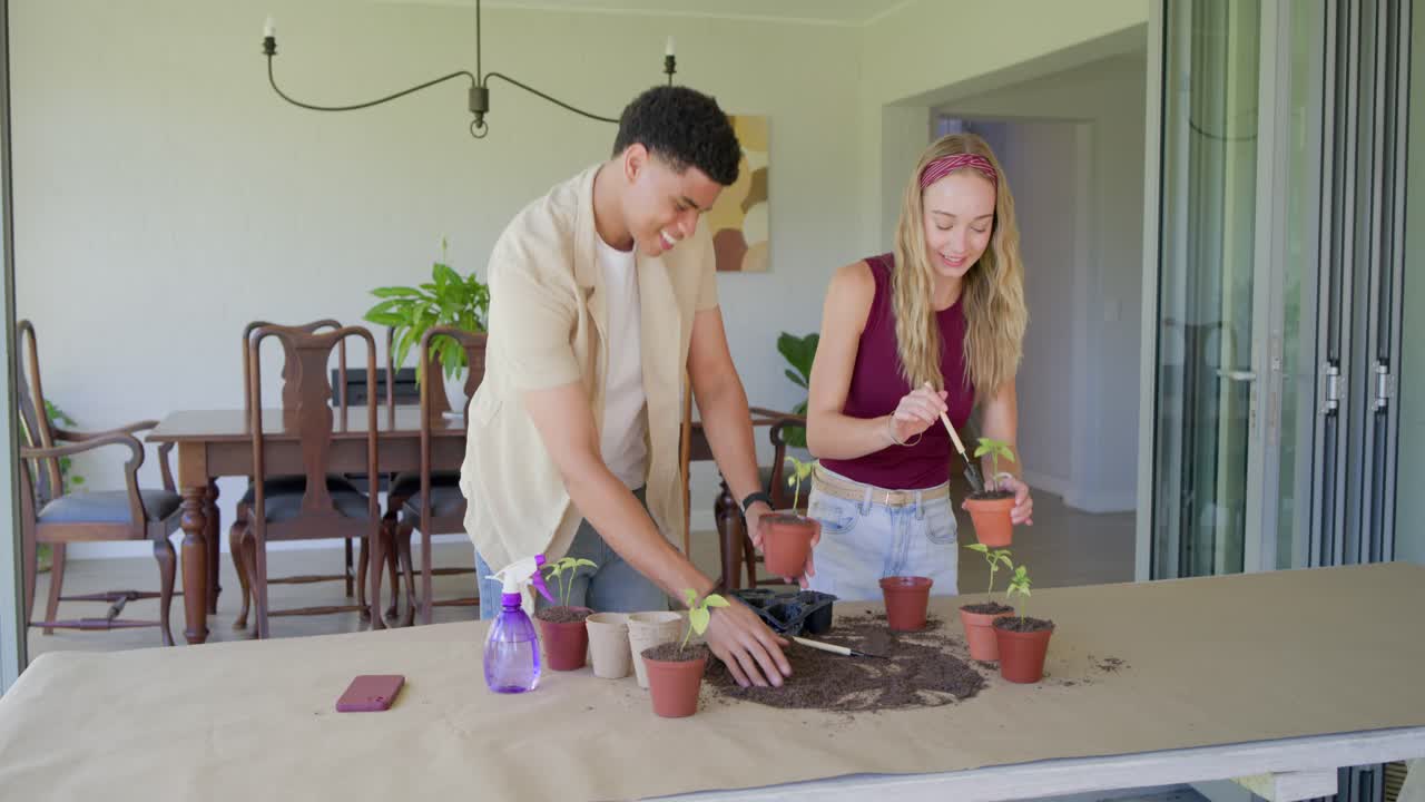 Casal diverso arrumando vasos e terra em mesa de pátio coberto, plantando mudas para horta doméstica