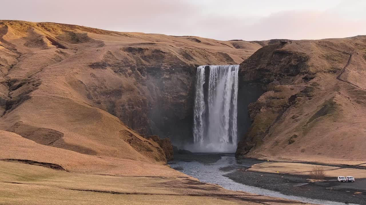 Frontal view of Skógafoss waterfall in Skógar, Iceland, with Skógá river plunging over a cliff into a misty basin. Majestic landscape near Eyjafjallajökull under soft light.