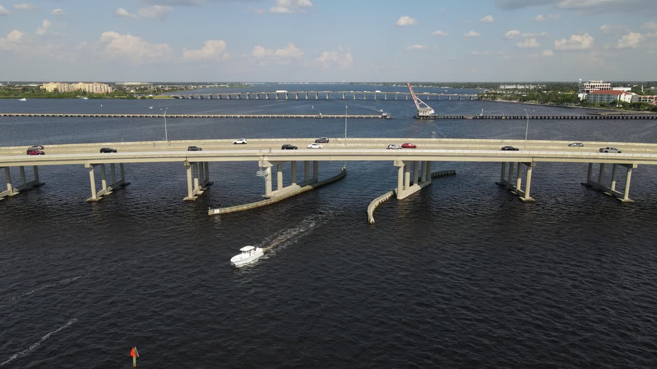 A boat passes beneath the Green Bridge in Bradenton, Florida, with cars traveling above. Crane Up