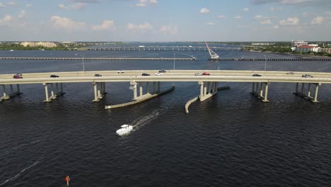 a boat passes beneath the green bridge in bradenton, florida, with cars traveling above. crane up