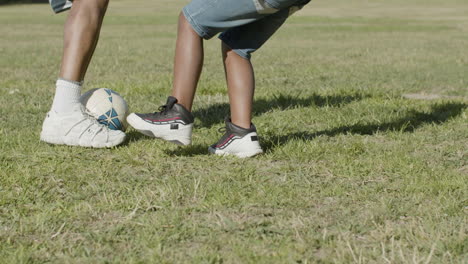 legs closeup of father and son playing football in summer park.