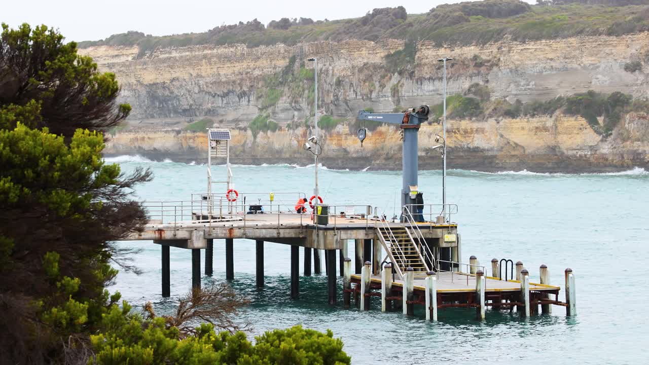 A serene view of a pier with people, set against coastal cliffs and calm waters, under soft daylight