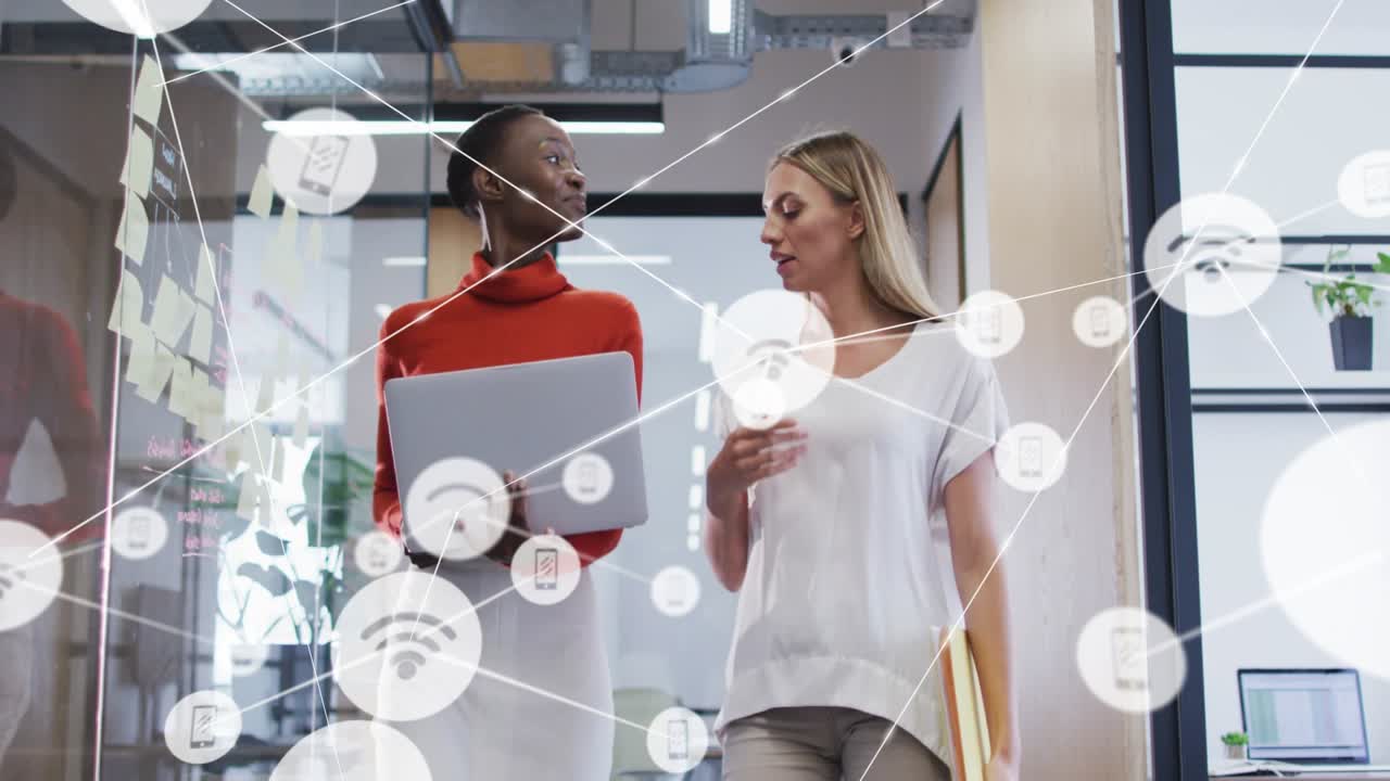 Two business women walking hall tilting laptop causing network overlay annotating data resuming