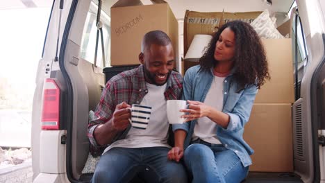 slow motion shot of couple taking a break in back of removal truck on moving day