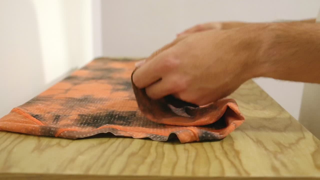 hombre plegando una camiseta en la parte superior de madera del cajón