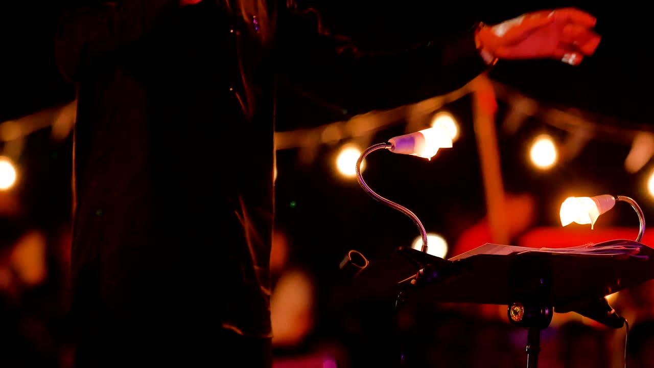 야외 야간 콘서트에서 교향악단 지휘자의 4k 손