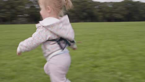 Happy-baby-girl-lying-on-the-grass-in-park-stands-up-and-runs-away-from-camera-during-summertime-UK-England