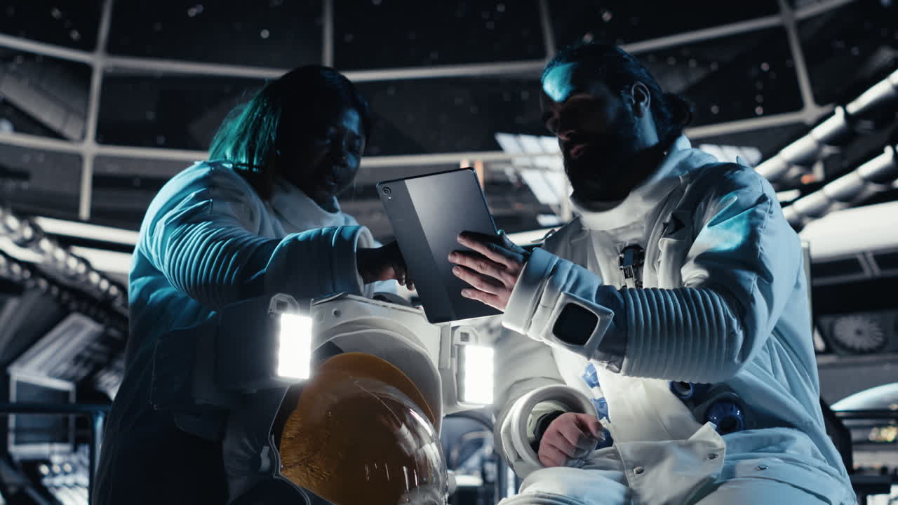 Astronaut reviewing onboard analytics on tablet, talking to colleague
