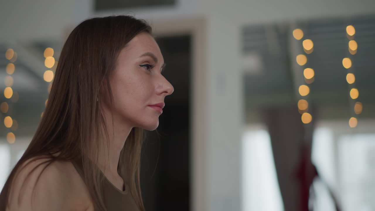 Side view yoga trainer stands on pink mat placing hands over chest and stomach with eyes closed gently in modern glass studio decorated with warm fairy lights for serene mindfulness session