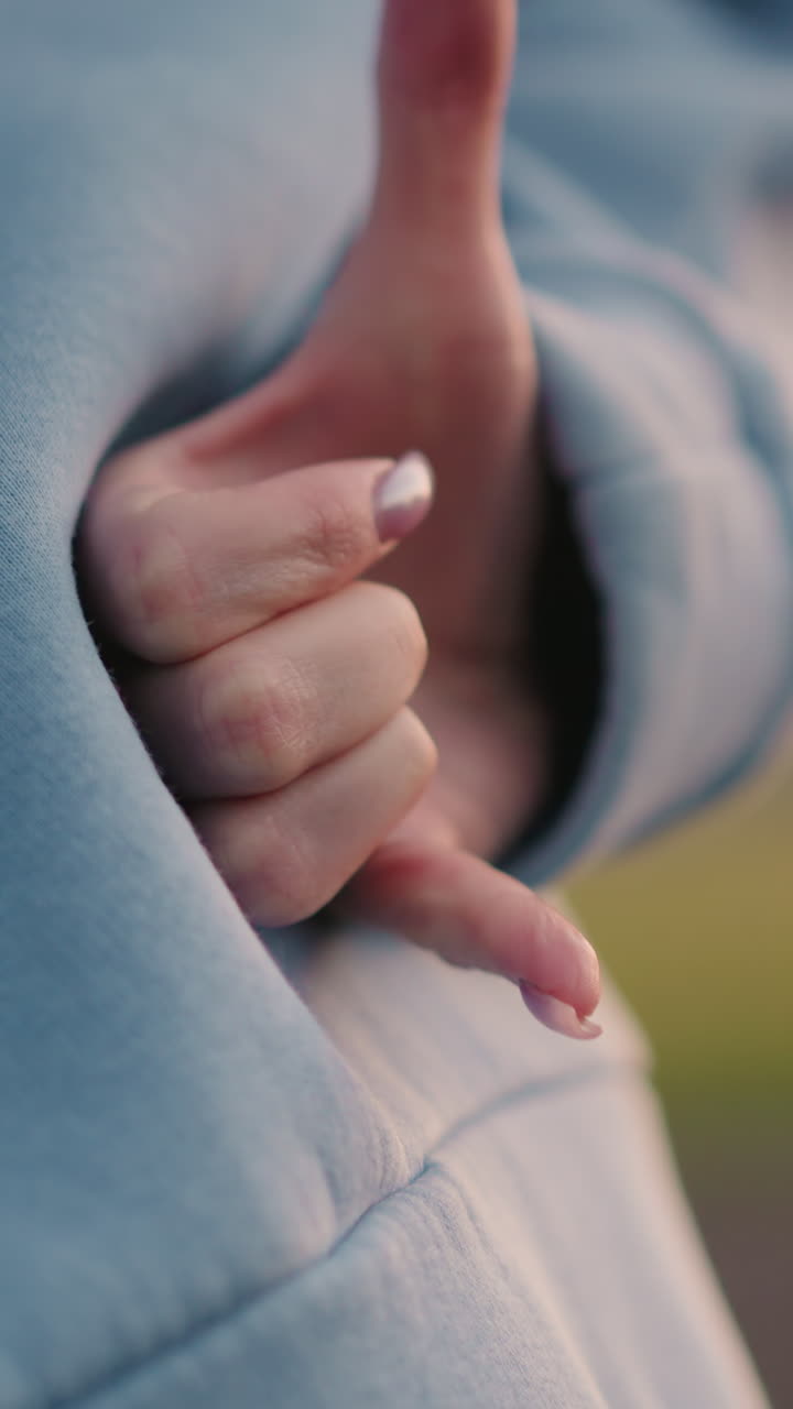 primer plano de una mujer con uñas pulidas llevadas a la cintura haciendo un gesto de la mano, vegetación borrosa en el fondo, destacando el entorno al aire libre tranquilo