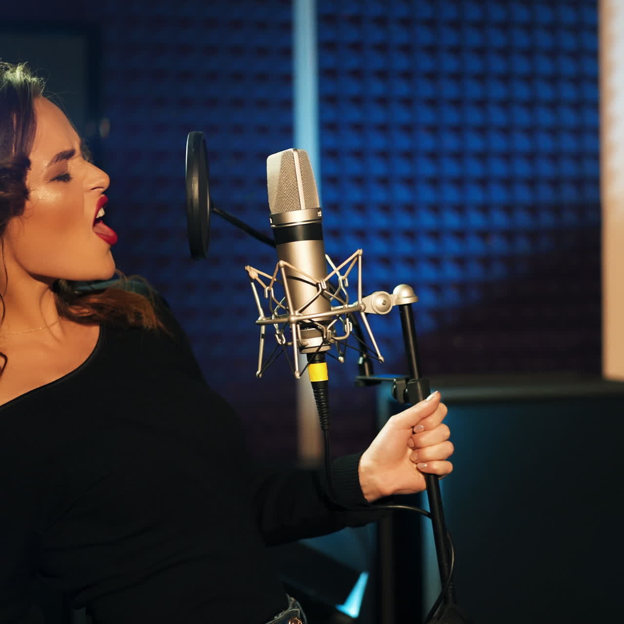 Girl singing to the microphone in a studio. Female vocal. Professional recording studio