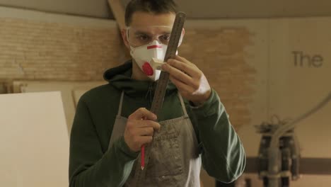 hardworking professional carpenter in mask and glasses holding a ruler