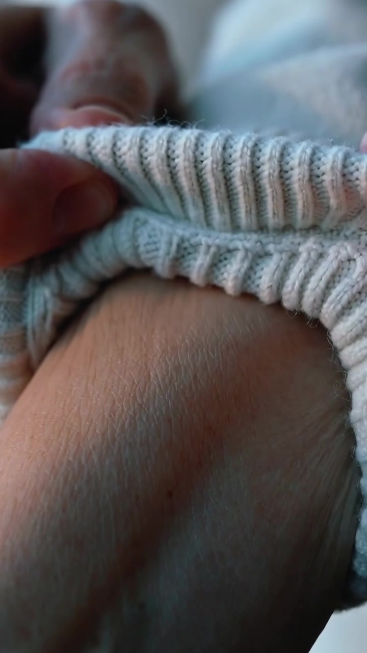 Video verticale: Mani che sollevano e tirano l'orlo di un maglione a costine in una stanza tranquilla, aggiustando e rivelando l'addome