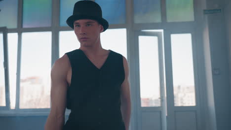 man in black vest and shirt spins in loft style studio, removes shirt mid dance and flings it with confident elegant expression against backlit windows and rising smoke haze and dramatic flair
