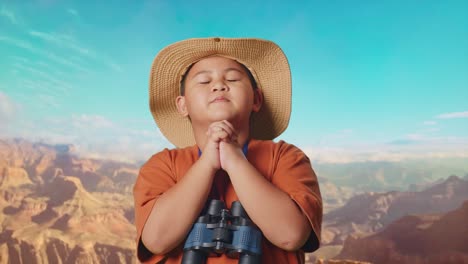 asian boy with a hat and binoculars praying for something while traveling at the top of mountain. boy researcher examines something, travel tourism adventure concept, close up
