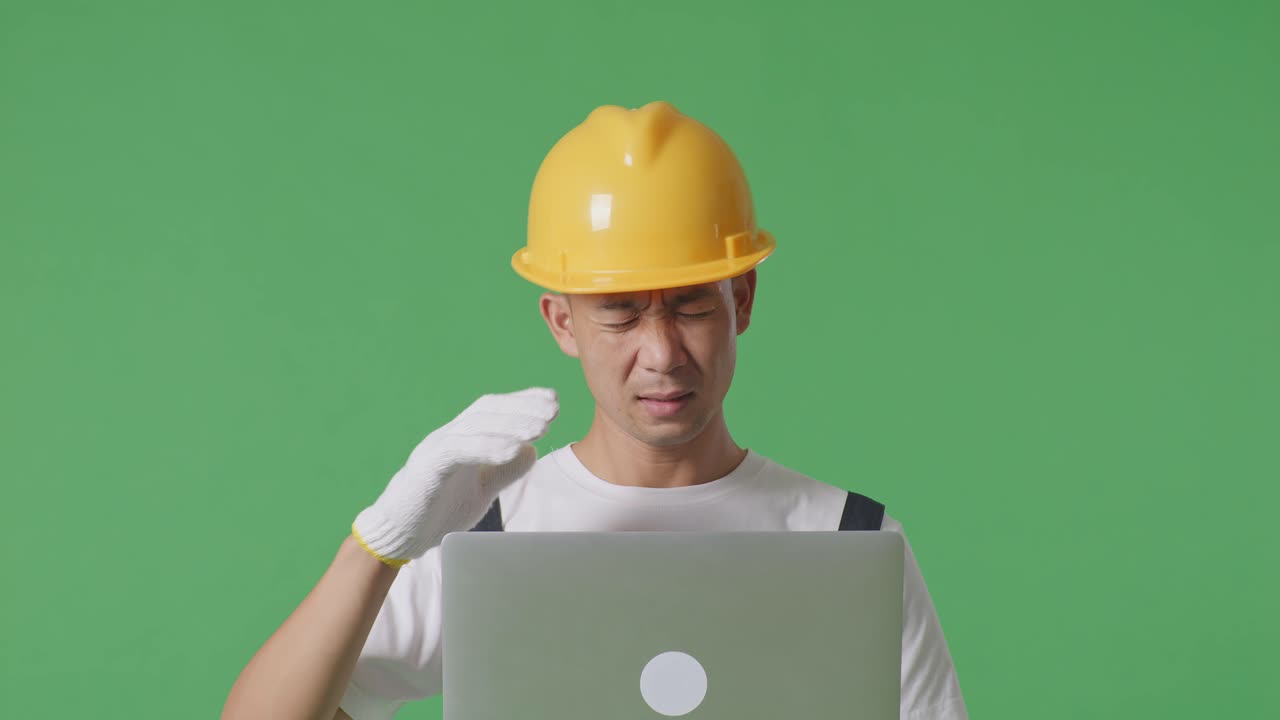 Close Up Of Asian Man Painter Wearing Safety Helmet Using A Laptop And Having A Headache While Standing In The Green Screen Background Studio