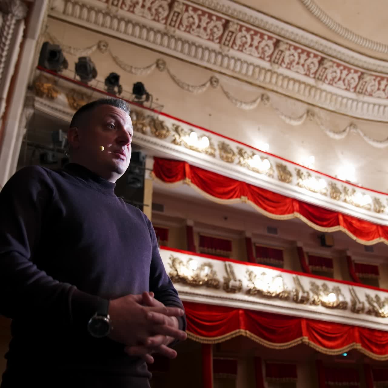 Man is giving interview in the opera house. Middle-aged actor talking to someone while standing on stage on classical theatre background