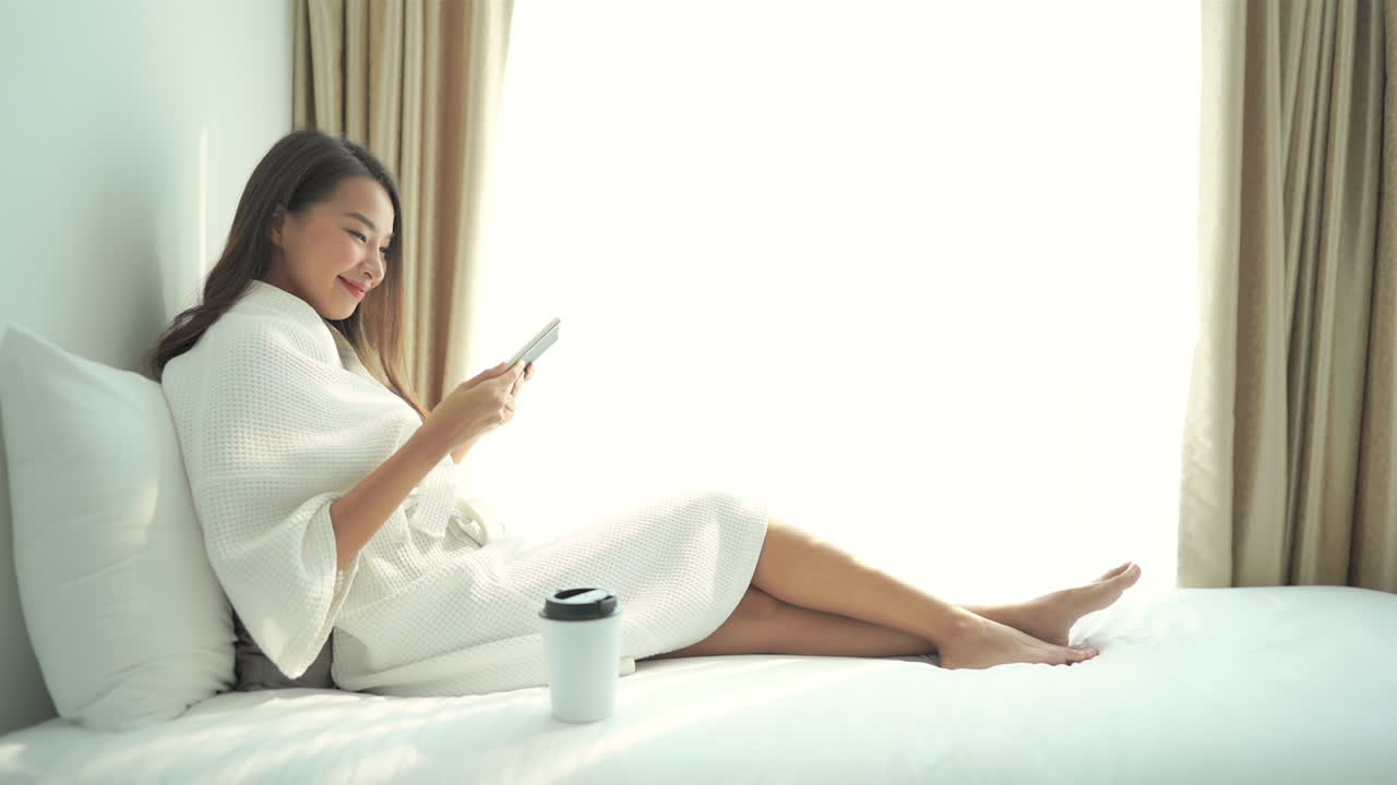 Woman in white bathrobe reading in bed, coffee time, morning routine