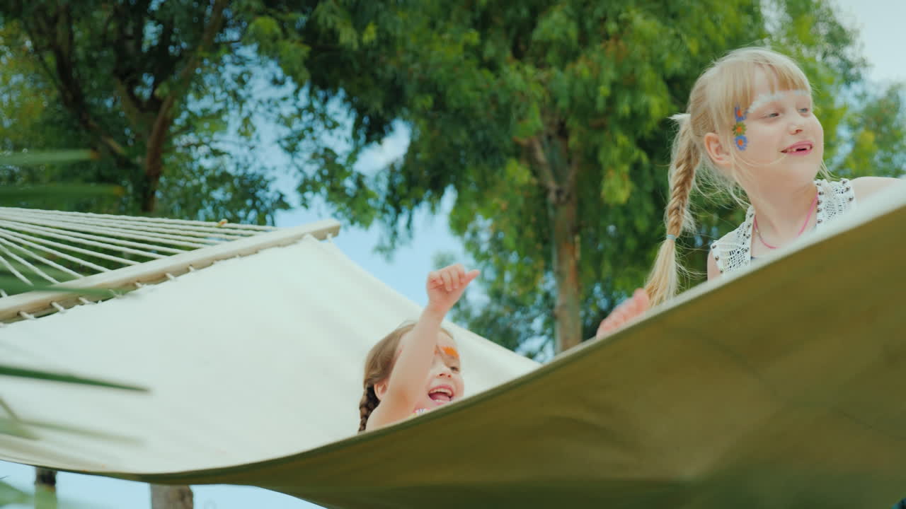 dos niños con caras pintadas se divierten en una hamaca ríen y disfrutan de las vacaciones