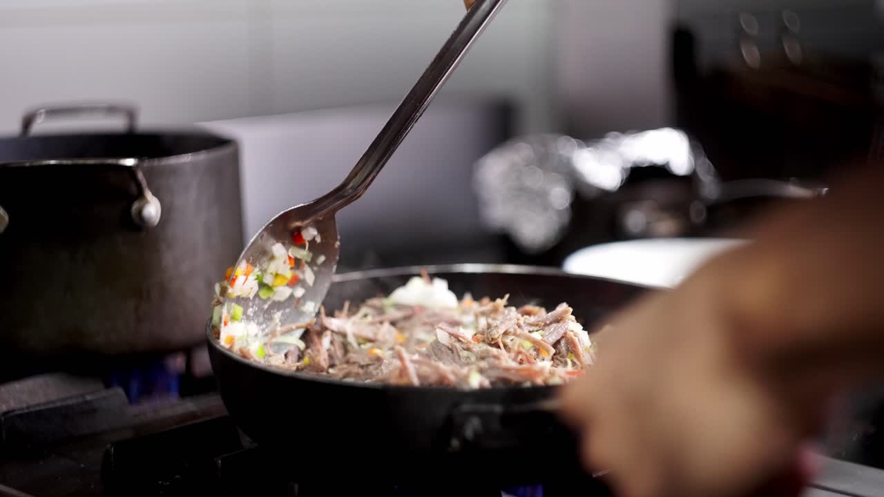 Close up view of a metal spoon stirring beef stew with vegetables in a pan in slow motion.