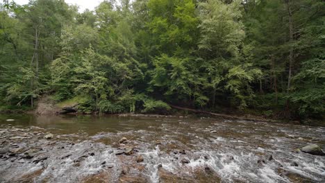 Wissahickon-Creek-flows-over-rocks,-stones,-trees-in-background